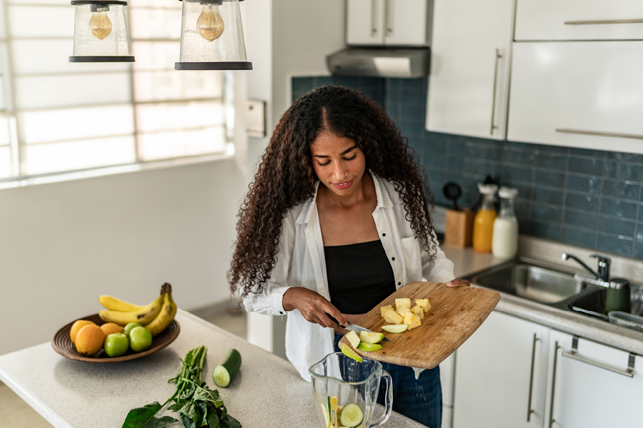 Woman smiling and making a smoothie in the kitchen.