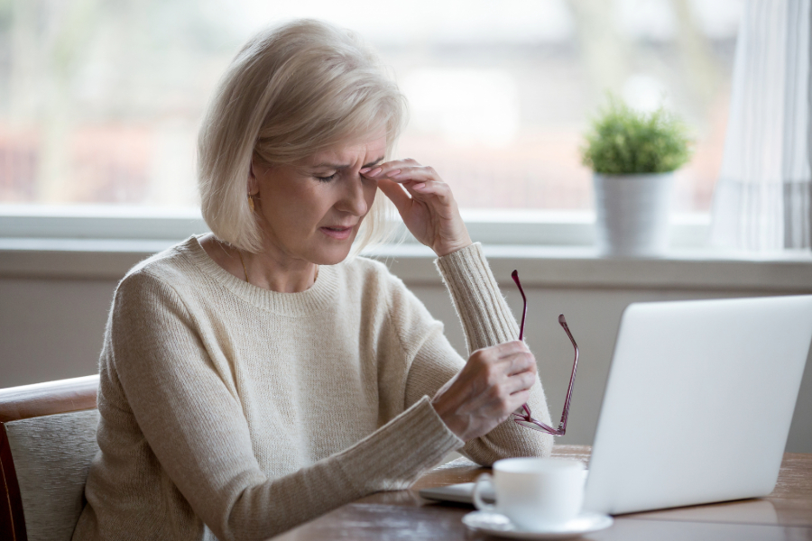 senior woman sitting in front of laptop rubbing sore eyes